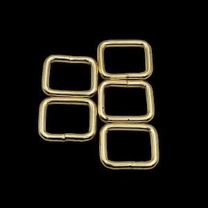 May include: Four gold-colored metal D-rings, stacked in a staggered pattern. The rings are smooth and have a polished finish.