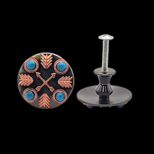Pode incluir: Dois puxadores decorativos para armários. Um é redondo com fundo preto e desenhos de flechas e folhas acobreadas, com detalhes turquesa. O outro puxador tem base preta e parafuso prateado.