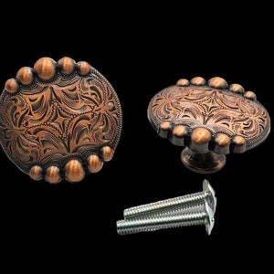 May include: Two copper-toned cabinet knobs with an ornate floral design and a rounded edge. The knobs have a decorative screw head and come with two screws.