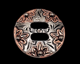May include: A silver and copper concho with a floral design and a double-slot opening. The concho has a polished finish and is decorated with small, round studs.