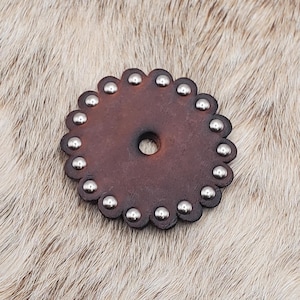 May include: A brown leather concho with a scalloped edge and silver studs.