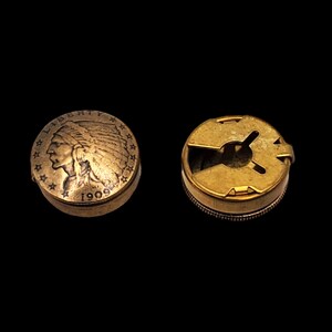 May include: A gold-colored coin with the profile of an indigenous person wearing a headdress and the year 1909 inscribed on it. The coin is on the left side of the image. On the right side of the image is a gold-colored metal button with a circular opening in the center.