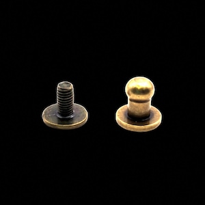 May include: Two antique brass-colored metal button fasteners. One fastener has a round head and the other has a screw head.