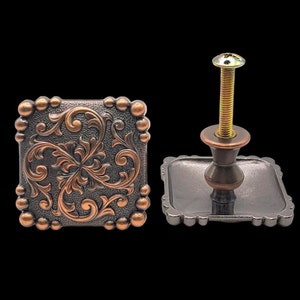 May include: A square cabinet knob with a decorative floral design in copper and black. The knob has a screw-on base.