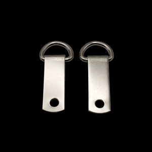 May include: Two silver metal D-ring picture hangers with a small hole in the center of each. The hangers are designed to be screwed into a wall to hang pictures.