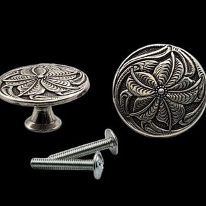 May include: Two silver cabinet knobs with a floral design. The knobs are round and have a raised design. The knobs come with two screws.