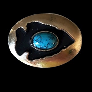 以下が含まれることがあります： 中央にターコイズブルーのcabochon石がついた、黒のエナメルデザインの銀製の楕円形のブローチです。