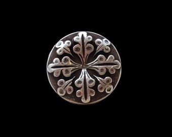 Op de afbeelding: Een zilveren ronde hanger met een gedetailleerd bloemmotief in de vorm van een kruis.