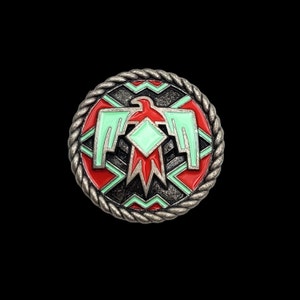 May include: A silver-toned metal button with a red, green, and black design. The design features a stylized eagle with a diamond shape in the center. The button has a rope-like border.