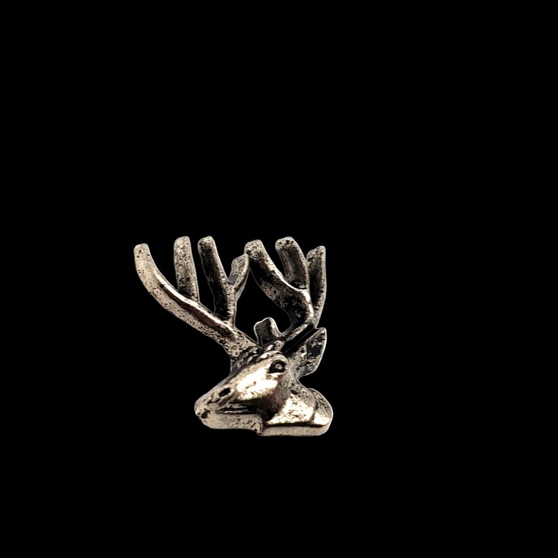 May include: A silver-toned deer head charm with antlers. The deer head is facing to the left and has a detailed design.