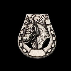 May include: A silver horseshoe charm with a detailed horse head design. The horseshoe is decorated with intricate patterns and the horse head is facing to the left.