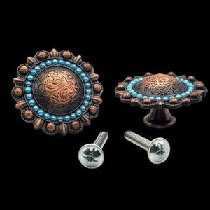 May include: Two ornate copper-toned cabinet knobs with a turquoise blue beaded trim and a swirling engraved design. The knobs are shown with two silver screws.