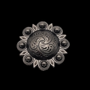 May include: A silver-toned metal concho with a decorative floral design. The concho has a circular shape with a raised center and a scalloped edge.