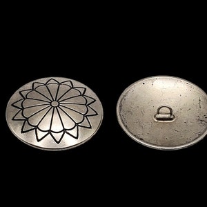 May include: A silver button with a decorative floral design on one side and a loop on the other side.