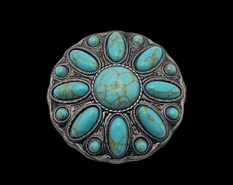 May include: A round, silver-toned belt buckle with a floral design. The buckle features a large, central turquoise stone surrounded by smaller turquoise stones. The stones have a marbled appearance and are set in a decorative metal frame.