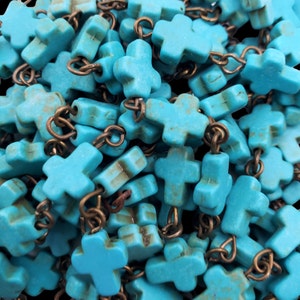May include: A close-up of a pile of turquoise blue cross-shaped beads with antique brass chain links. The beads are strung together to create a necklace or bracelet.