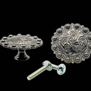 Pode incluir: Dois botões de armário de metal prateados com um design floral decorativo. Um botão tem uma base elevada e o outro é plano. Um parafuso prateado está incluído.