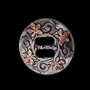 May include: A silver and copper floral concho with a double-slot design. The concho is circular in shape with intricate floral patterns and a copper finish on the flowers.
