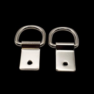 May include: Two silver metal D-rings with a rectangular plate attached to each ring. The plates have a small hole in the center.