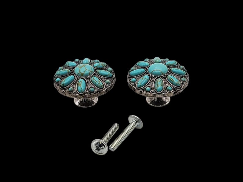 Może przedstawiać: Dwa dekoracyjne gałki do szafek ze srebrnym wykończeniem i inkrustowanymi turkusowymi kamieniami. Gałki mają kwiatowy wz&oacute;r i towarzyszą im dwie srebrne śruby, wszystko na czarnym tle.