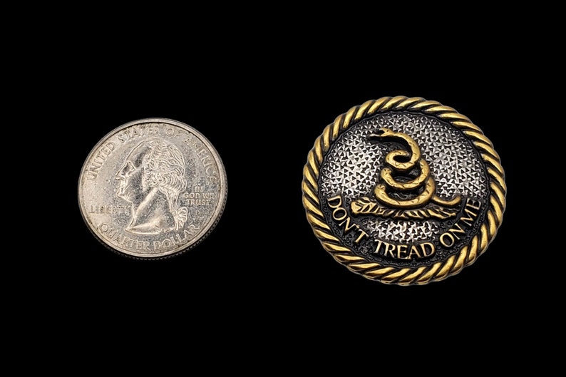 May include: A gold-colored metal button with a black and white textured background. The button features a gold-colored snake with the text "Don't Tread On Me" around the snake.