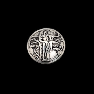 May include: A silver half dollar coin depicting a Native American figure with outstretched arms. The coin is circular, with the words "UNITED OF HALF STATES AMERICA DOLLAR" around the edge. The coin is set against a black background.