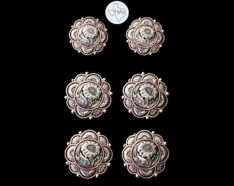 May include: Six circular metal conchos arranged in three pairs, each featuring a central embossed floral design surrounded by a scalloped edge with a copper-toned finish. A small white circular logo with a Texas outline and the letters HAJ is centered above.