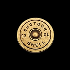 Peut inclure: Une douille de fusil de chasse dorée avec le texte "SHOTGUN SHELL 12 GA" en relief sur le côté.