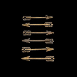 May include: Seven gold-toned arrow charms with a textured surface. The arrows are arranged vertically in a row.