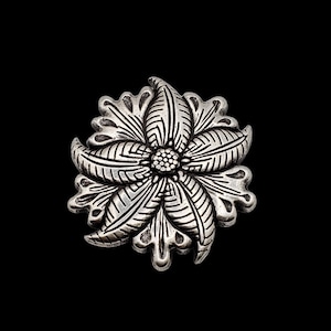 Op de afbeelding: Een zilveren broche in de vorm van een bloem met ingewikkelde details en een getextureerd oppervlak.