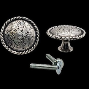 May include: Silver-toned cabinet hardware set, featuring two decorative knobs and two screws. The knobs have a detailed floral and swirl design, with a rope-like border. The hardware is set against a black background.