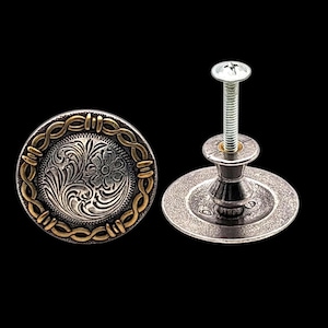 May include: Two silver and gold cabinet knobs with a western design. The knobs have a floral pattern in the center and a gold rope-like border. One knob is attached to a screw.