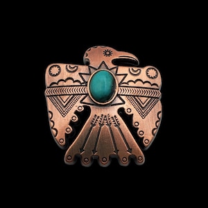 Pode incluir: Um alfinete de metal de cor cobre com uma pedra turquesa no centro. O alfinete tem a forma de um pássaro estilizado com desenhos geométricos intrincados.