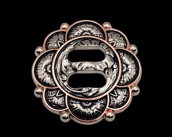 May include: A silver and rose gold metal concho with a floral design. The concho has two holes in the center.