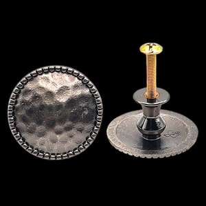 May include: A black metal cabinet knob with a hammered finish and a beaded edge. The knob has a round base and a screw for installation.