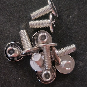 May include: A close-up of a pile of silver-toned screws with flat heads and washers. The screws are arranged in a random pattern.