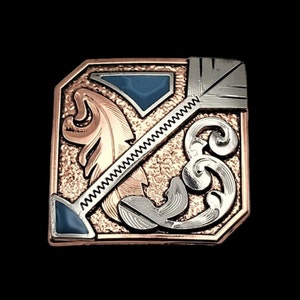 以下が含まれることがあります： 羽根、矢、花柄の複雑なデザインが施された、正方形のシルバーとローズゴールドのベルトバックル。バックルには青い石のインレイが施されています。