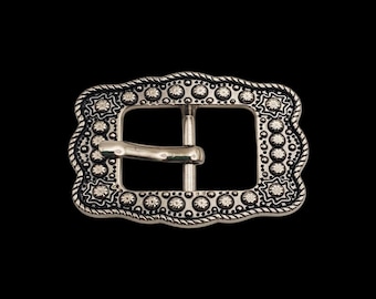 May include: A rectangular silver-toned belt buckle featuring a rope-textured border and an intricate pattern of embossed star-like motifs and small raised dots surrounding the central opening, complete with a smooth, curved metal prong.