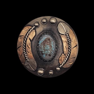 May include: A round button made of silver and gold, featuring a turquoise stone at its centre. The button is adorned with a feather design and has a textured surface.