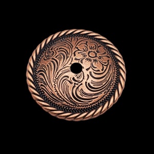 May include: A copper-colored metal button with a rope-like border and an intricate floral design. The button has a hole in the center.
