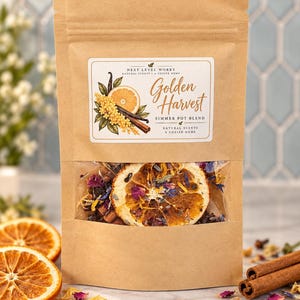 May include: A brown kraft paper pouch containing a Golden Harvest simmer pot blend. The label features illustrations of orange slices, cinnamon sticks, and yellow flowers. A clear window reveals dried orange slices, petals, and spices inside.