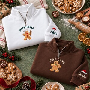 May include: A white quarter-zip sweatshirt embroidered with a gingerbread person and the text "COOKIE BAKER" and a brown quarter-zip sweatshirt embroidered with a gingerbread person and the text "COOKIE TESTER", both featuring personalized names on the sleeve.