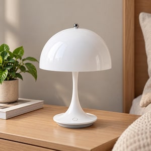 May include: A white mushroom-shaped table lamp with a glossy dome shade and a slender, flared base. The lamp features a small metallic silver sphere at the very top of the dome and a circular power button located on the front of the base.
