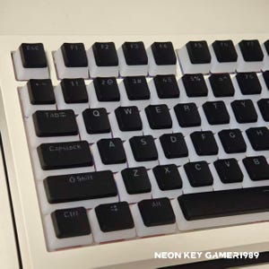 May include: A computer keyboard featuring black keycaps with white translucent sides and white lettering. The keys include standard QWERTY layout, function keys, and control keys. The text NEON KEY GAMER1989 is visible in the bottom right corner.