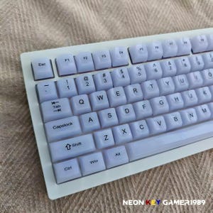 May include: A white mechanical keyboard featuring translucent keycaps with black lettering in a standard QWERTY layout. The keyboard includes function keys, a numeric row, and standard modifier keys like Esc, Tab, Capslock, Shift, Ctrl, Win, and Alt.