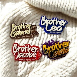 May include: Four custom acrylic pins featuring names and fraternity affiliations. One brown pin reads Brother Gabriel Iota Phi Theta, one blue pin reads Brother Leo Phi Beta Sigma, one red pin reads Brother Jacobe Kappa Alpha Phi, and one purple pin reads Brother Caleb Omega Phi Psi.