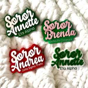 Peut inclure: Quatre badges nominatifs personnalisés avec des designs en acrylique superposés. Les badges affichent le texte Soror Annette Eta Alpha, Soror Brenda Beta Pi Omega, Soror Andrea Delta Sigma Theta et Soror Annette Eta Alpha en diverses couleurs.
