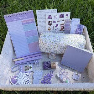 Peut inclure: Un ensemble de papeterie dans un panier, comprenant un agenda journalier violet, une trousse à motifs floraux, deux stylos violets, un petit carnet violet, une breloque panda, un porte-clés fleur, des trombones violets, des autocollants et un tampon.