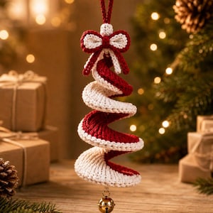 May include: A spiral-shaped hanging ornament crafted from red and white yarn, featuring a crochet texture. The ornament is topped with a small red and white bow and has a gold-colored metal bell attached to the bottom point for a festive appearance.