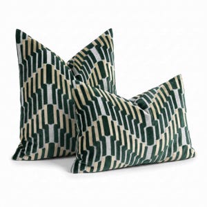 May include: Two decorative throw pillows featuring a repeating geometric pattern in deep forest green, cream, and light gray. The fabric has a soft, velvet-like texture with a structured, angular design that creates a sense of depth and movement.